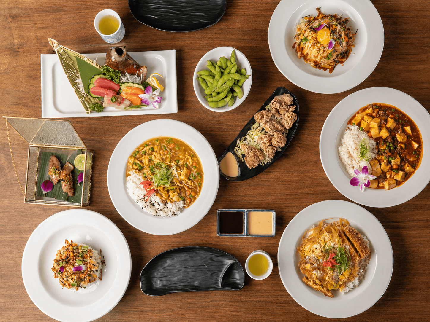 A spread of Ajisai lunch dishes including sashimi, curry rice, mapo tofu, chicken katsu, and poke don on a warm wood table